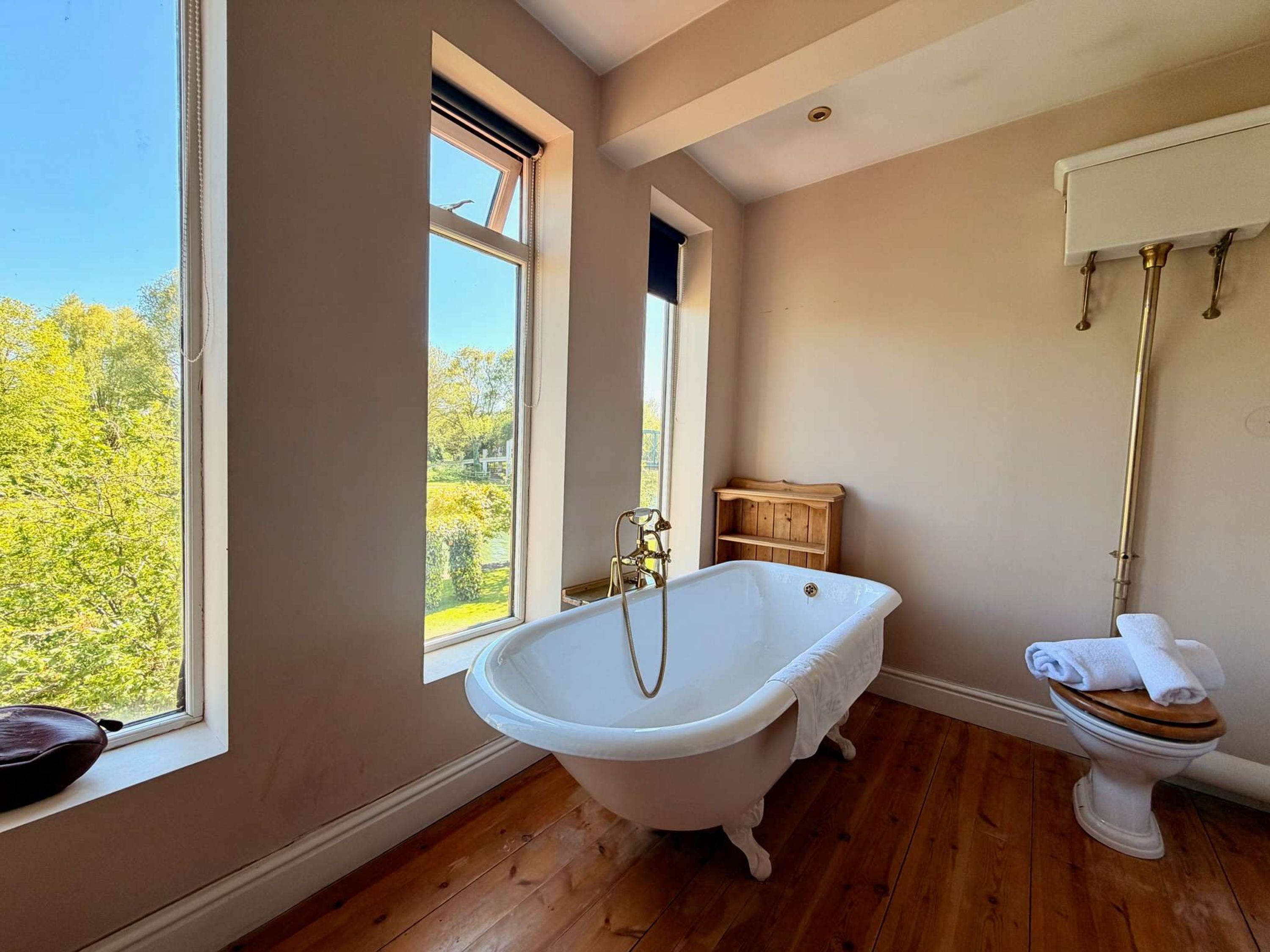 A bathroom with a freestanding bathtub, a toilet, and a window providing a view of trees.