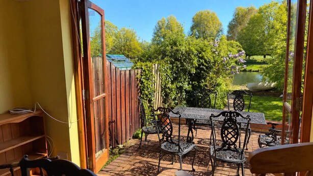 An open patio with a wooden table and chairs, a wooden fence, and a view of a garden with a pond. - The Boat Hole - Riverside Living in Cambridge (Cambridge)