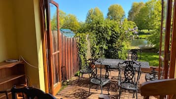 An open patio with a wooden table and chairs, a wooden fence, and a view of a garden with a pond.