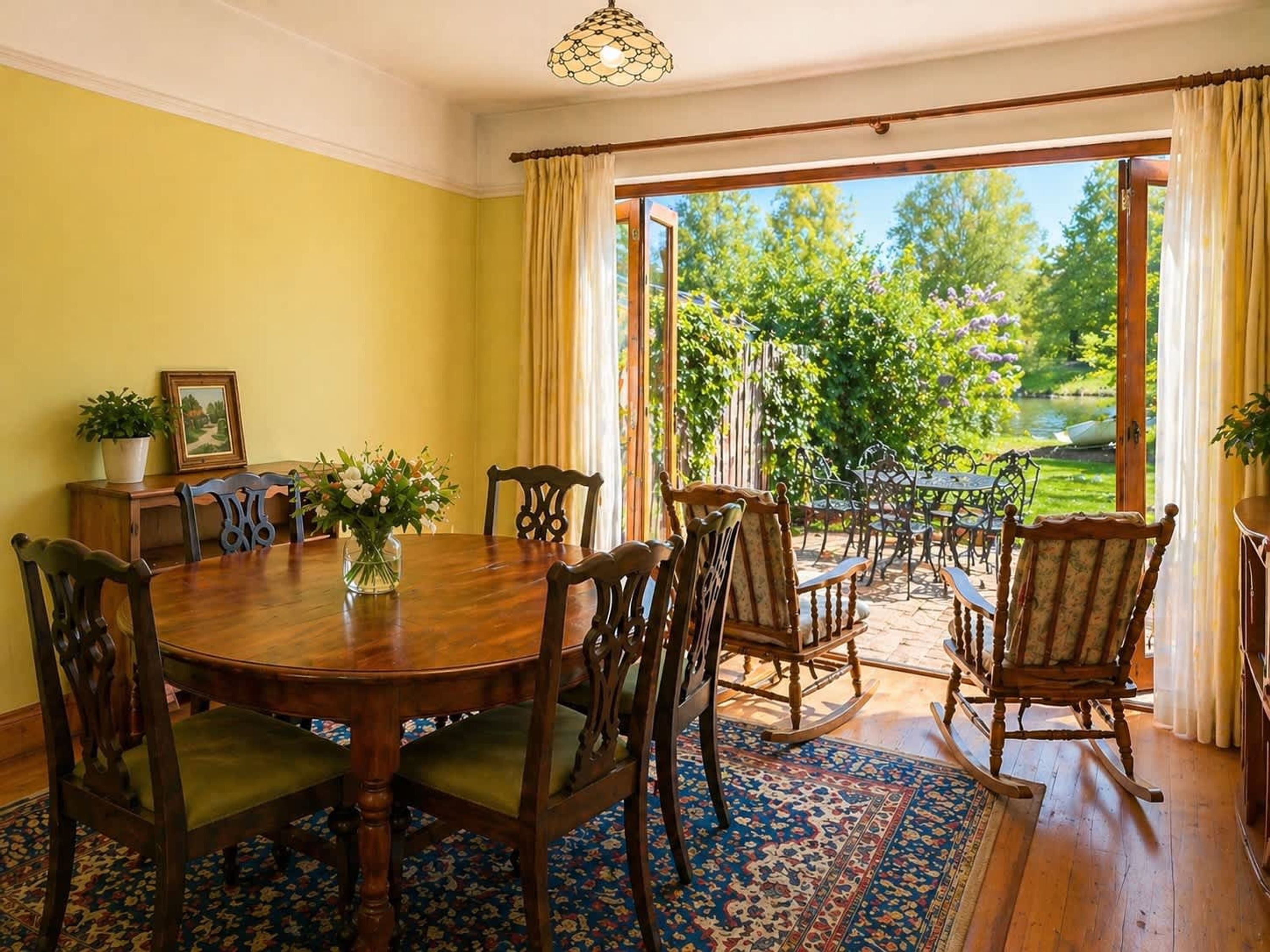 A dining area with a round table, chairs, and a view of a garden through a glass door.
