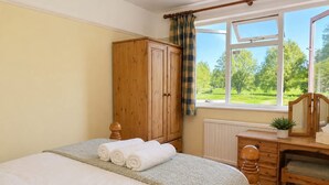 A bedroom with a bed, a wooden wardrobe, a desk with a mirror, and a window with a view of greenery. - The Boat Hole - Riverside Living in Cambridge (Cambridge)