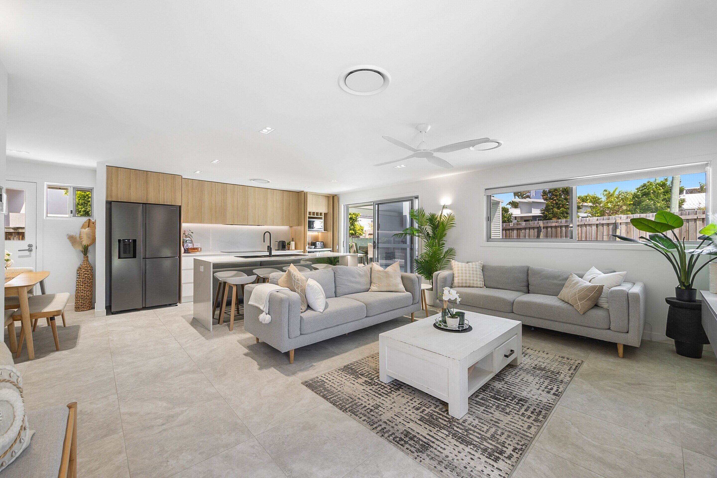 A modern living room with a sofa, coffee table, and a kitchen area with a refrigerator and dining table.