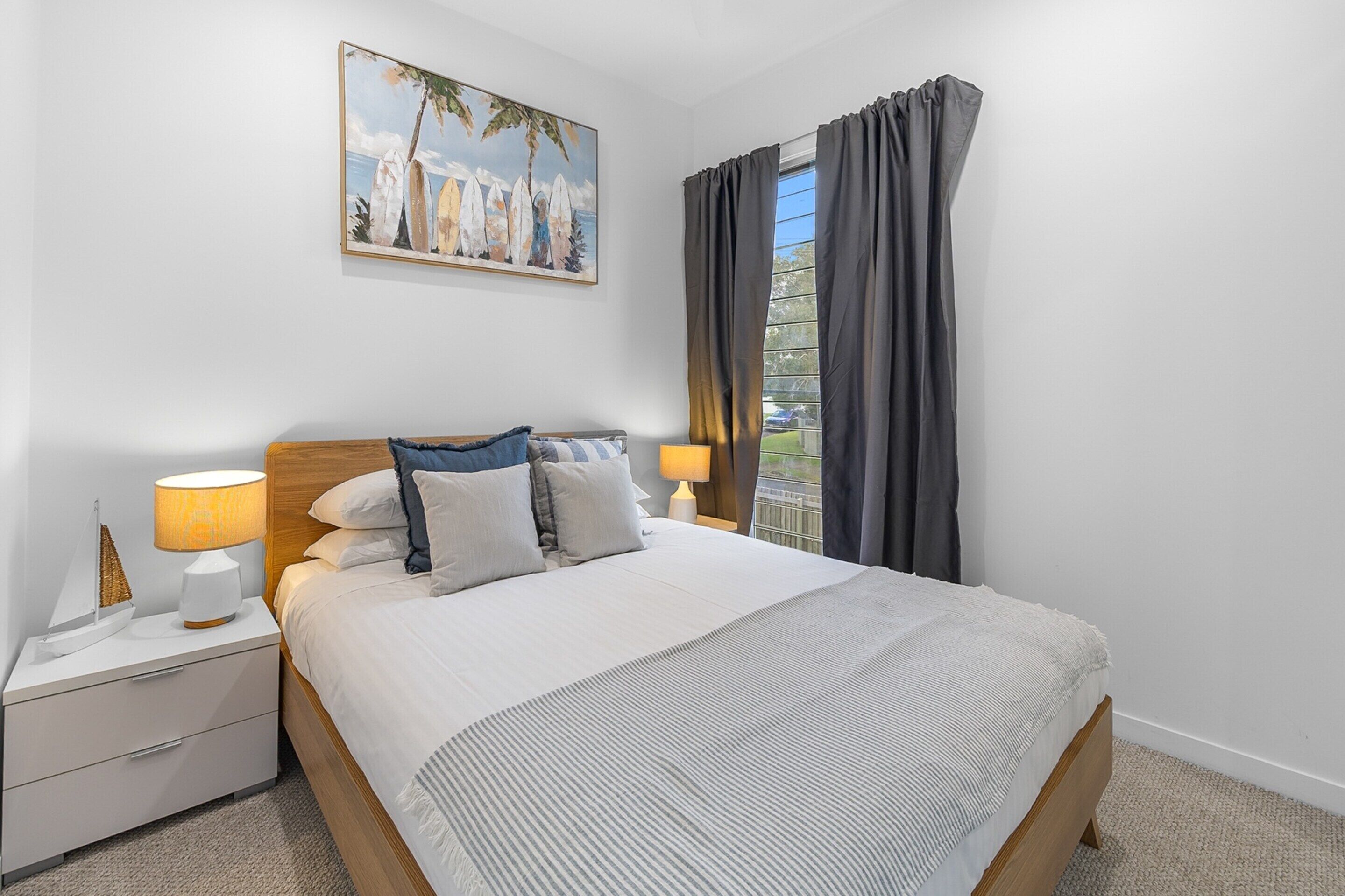 A neatly made bed with a headboard, a bedside table with a lamp, and a painting on the wall.