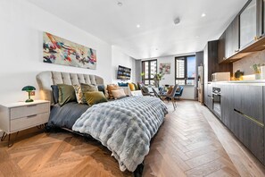 Ein modernes Schlafzimmer mit einem großen Bett, einem Fernseher, einem Schreibtisch und einer Küchenzeile.