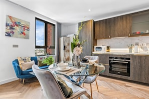 Eine moderne Küche mit Einbauofen, ein Essbereich mit Glastisch und ein blaues Sofa.