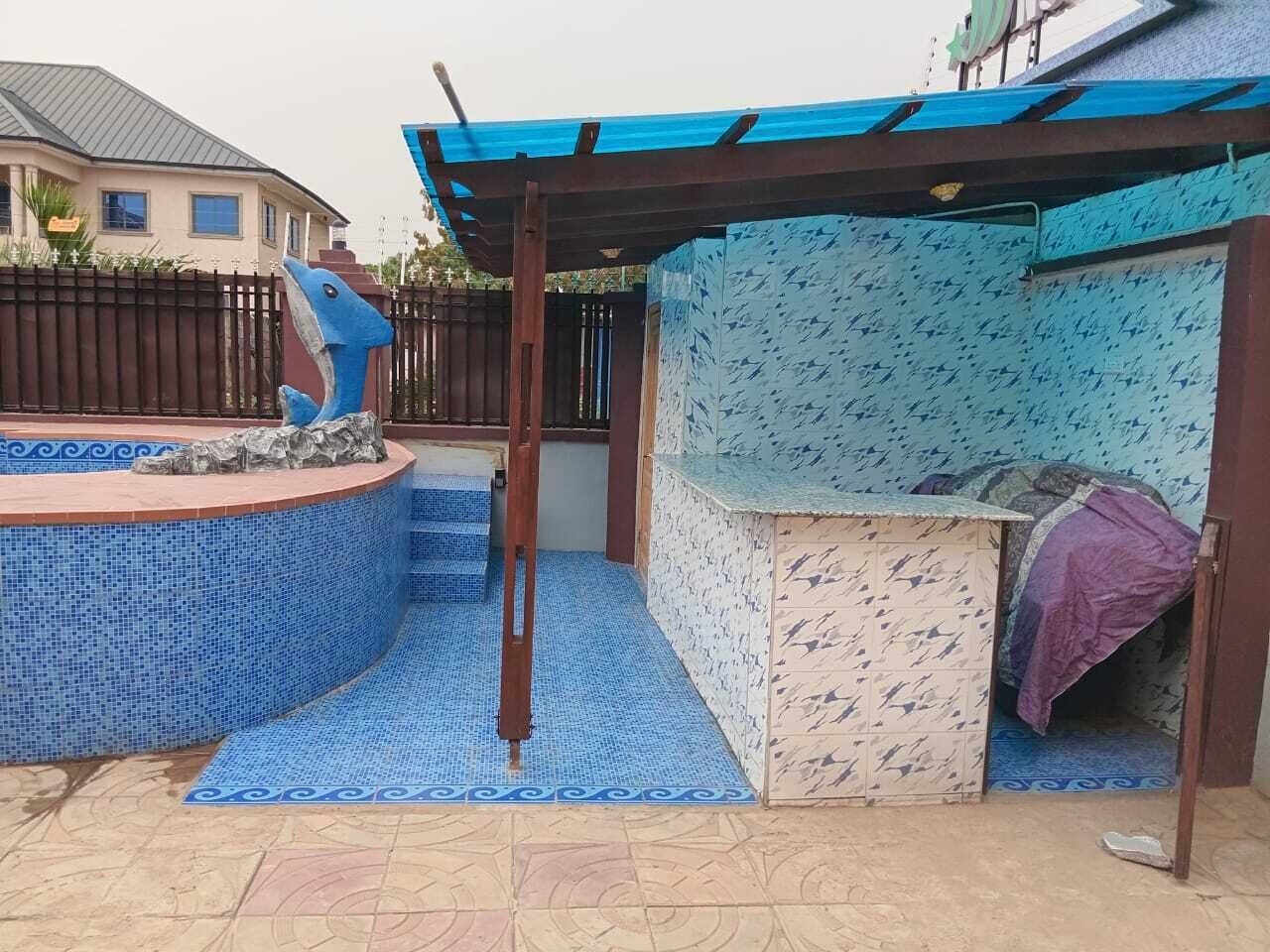 A covered outdoor area with a blue-tiled pool, a wooden bench, and a patterned wall.