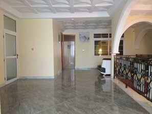 Un pasillo amplio con piso de mármol, techo blanco con diseño decorativo y barandal negro con detalles amarillos.