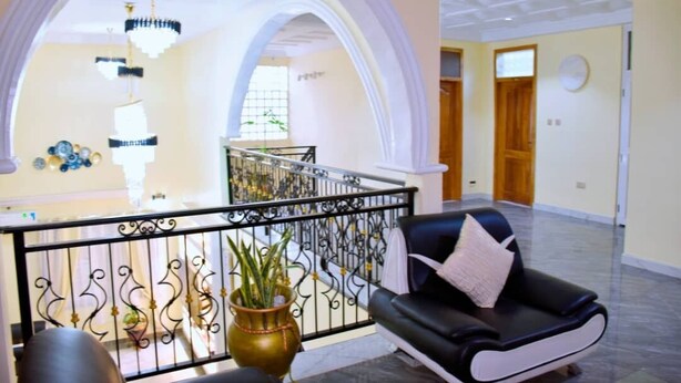 Un hall d’entrée spacieux, avec un canapé en cuir noir, une rampe décorative en métal et un escalier menant à l’étage supérieur.