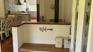 Una cocina moderna con una isla central, un comedor con sillas, un letrero que dice 'Welcome' y un recipiente para pienso.