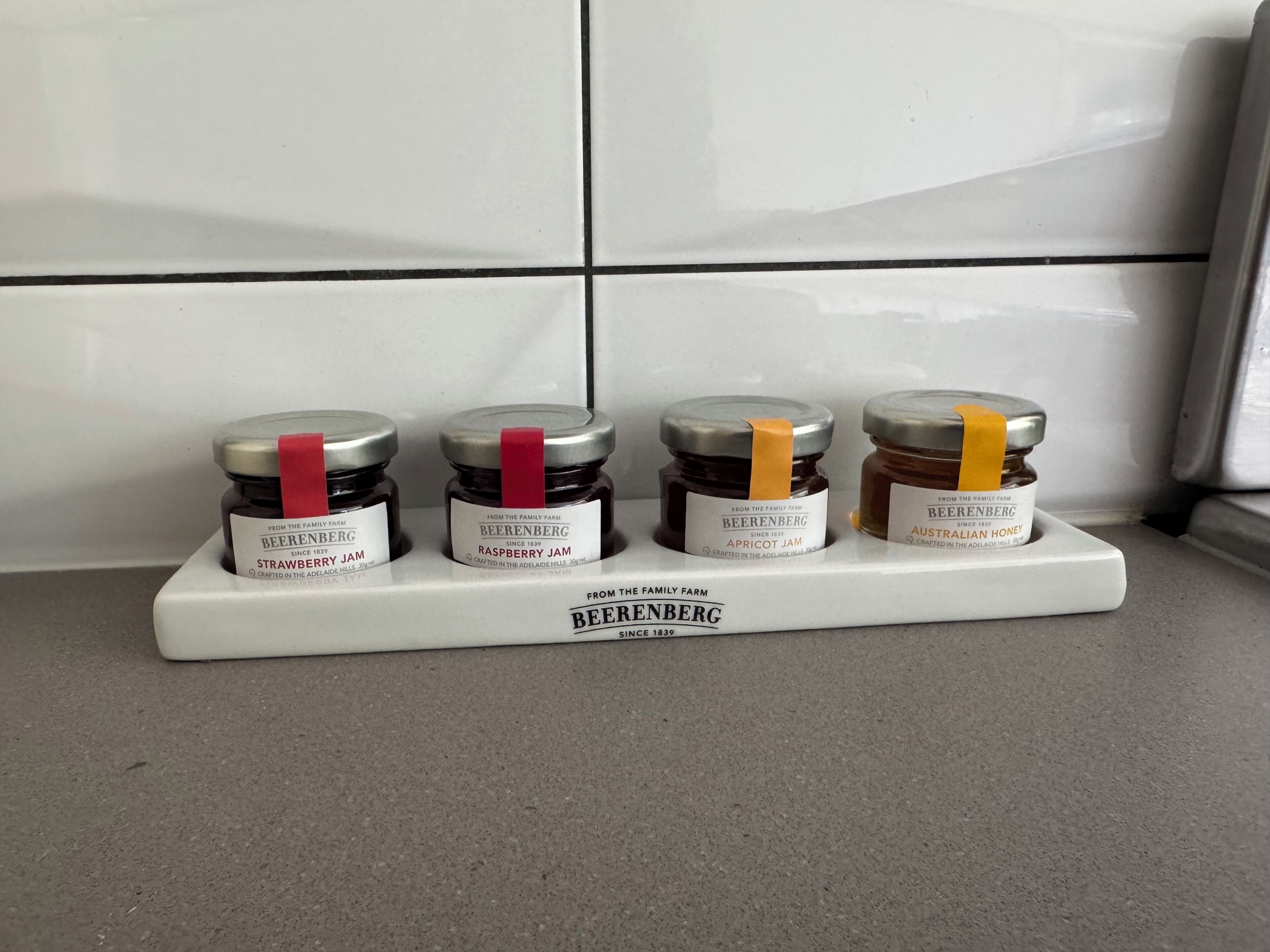 Vier potjes jam op een witte schaal, geplaatst op een aanrecht.