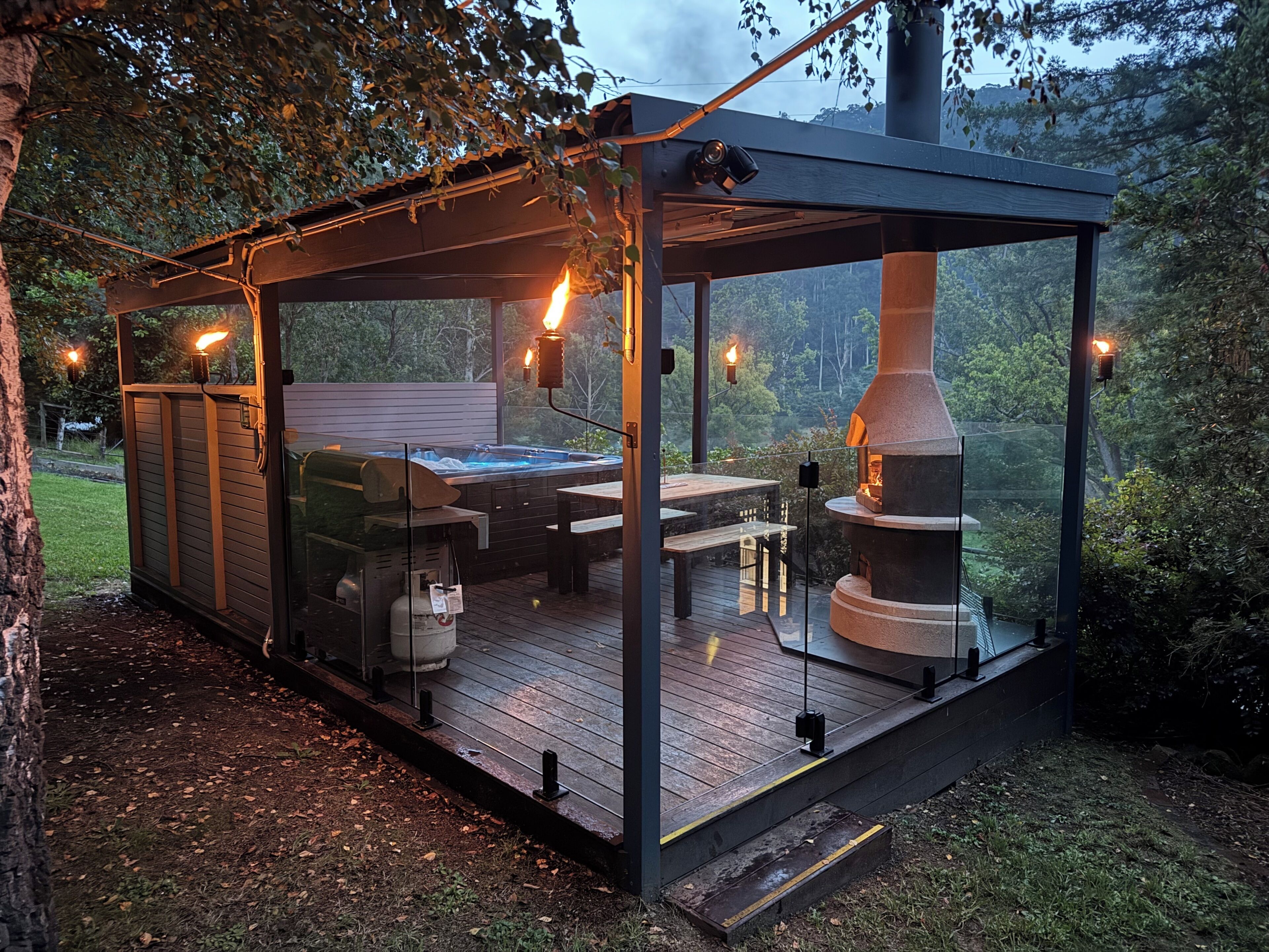Et udekøkken med glasfacade, indeholdende en brændeovn, et spabad og en grill.