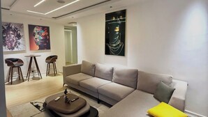 A modern living room with a sectional sofa, a coffee table, and two bar stools. - EIO SHORTLET (Abuja)