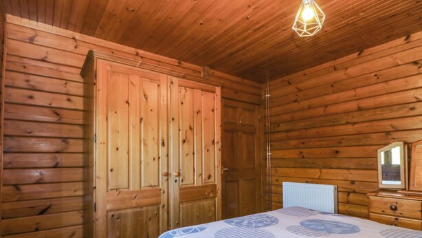 A wooden cabin bedroom with a bed, a wardrobe, and a mirror. - Lodge 9 - Bron Eifion (Criccieth)