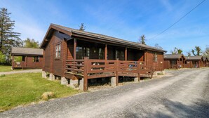 A rustic wooden cabin with a porch, a gravel driveway, and a clear blue sky. - Lodge 9 - Bron Eifion (Criccieth)