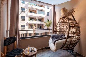 A balcony with a hanging chair, a small table with a drink and snacks, and a view of a multi-story building. - Menara Garden - 5 minutes from M'avenue - Pool view (Marrakesh)