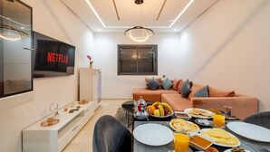 Moderni olohuone, jossa on sohva, sohvapöytä ja televisio, jonka näytöllä näkyy teksti ”NETFLIX”.