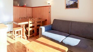 A living room with a sofa, wooden dining table, chairs, and a painting on the wall. - Family Apartment in La Foux D'allos (Allos)