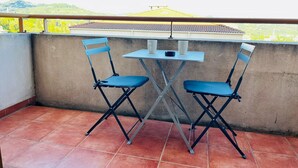 Un balcon avec deux chaises pliantes bleues et une petite table sur laquelle se trouve une lampe.