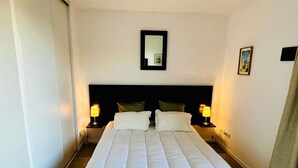 Une chambre d’hôtel avec un grand lit, deux lampes de chevet, une tête de lit, un miroir et un tableau au mur.