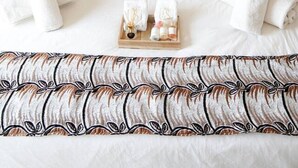 Una cama bien hecha con almohadillas estampadas y un atril con artículos de tocador.