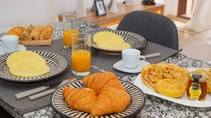 Una mesa de desayuno con cruasanes, un plato de huevos y zumo de naranja.