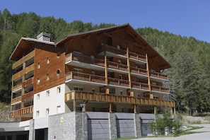 Ein mehrstöckiges Hotel mit Balkonen, einem Steinsockel und einer Bergkulisse.
