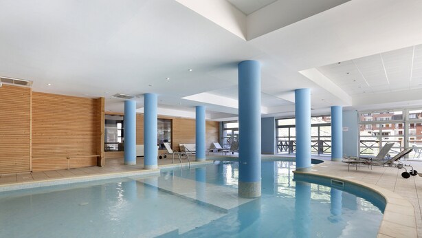 An indoor swimming pool with blue pillars, lounge chairs, and a wooden wall. - La Foux D'allos - Les Chalets du Verdon (Allos)