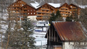 A multi-story wooden lodge with balconies, surrounded by snow-covered trees and a small cabin with a rusted roof. - La Foux D'allos - Les Chalets du Verdon (Allos)