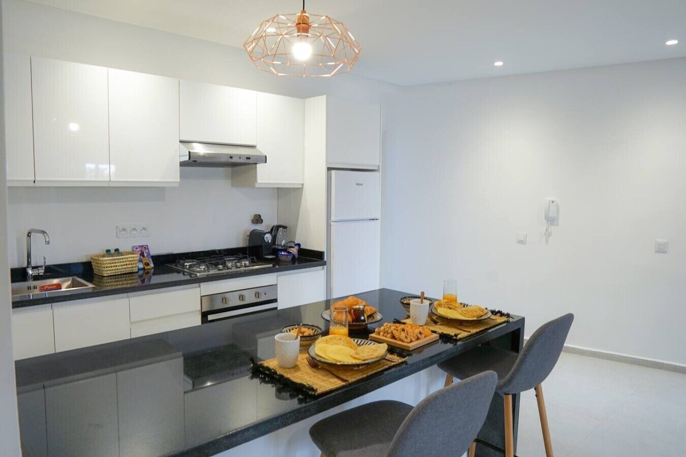 Een moderne keuken met een centraal eiland, roestvrijstalen apparatuur en een geometrische hanglamp.