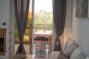 Ein Zimmer mit Holztisch und Stühlen, einer Couch, einem Kamin und einem Balkon mit Blick ins Grüne.