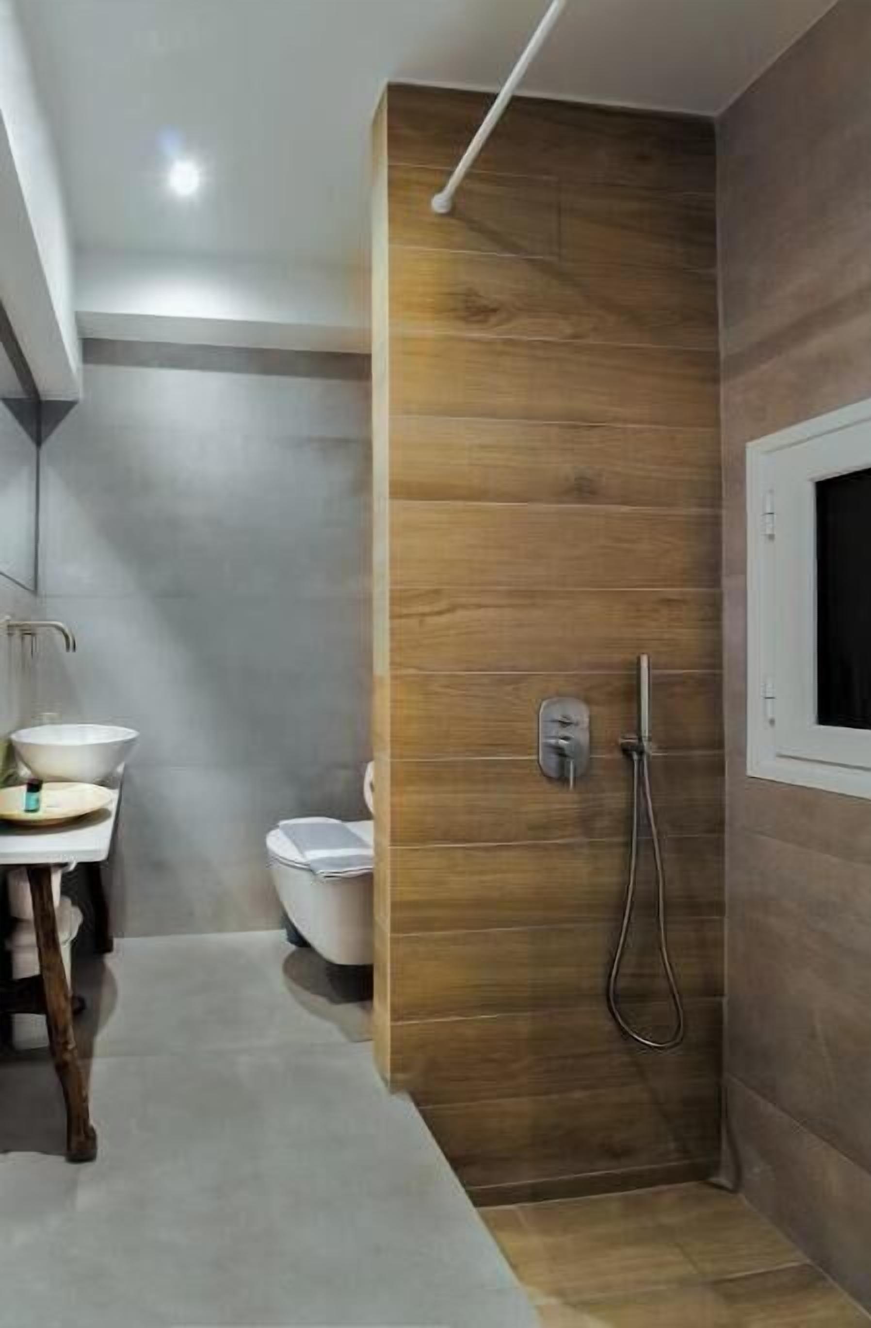 A modern bathroom with a wooden accent wall, a white sink, a toilet, and a shower area.