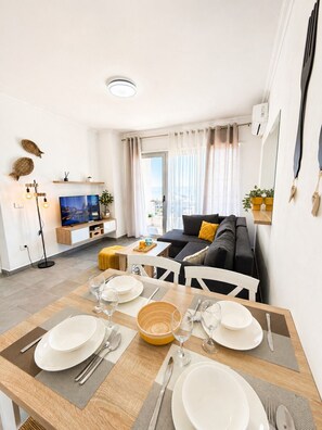 Ein modernes Wohnzimmer mit Essbereich, gedecktem Tisch, einem Flachbildfernseher und Blick auf die Stadt.
