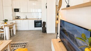Een moderne keuken met witte kastjes, een magnetron en een eethoek met een houten tafel en een geel poufje.