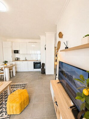 Eine moderne Küche mit weißen Schränken, einer Mikrowelle und einem Essbereich mit einem Holztisch und einem gelben Pouf.