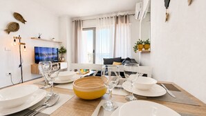 Een eetruimte met een tafel voor vier personen, een televisie op de achtergrond en een raam met gordijnen.