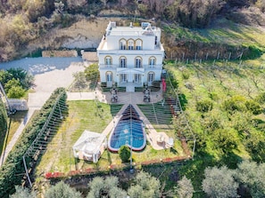 A large, white, multi-story building with a symmetrical facade, a swimming pool, and a well-maintained garden. - The Secret Garden Villa (Durrësi)