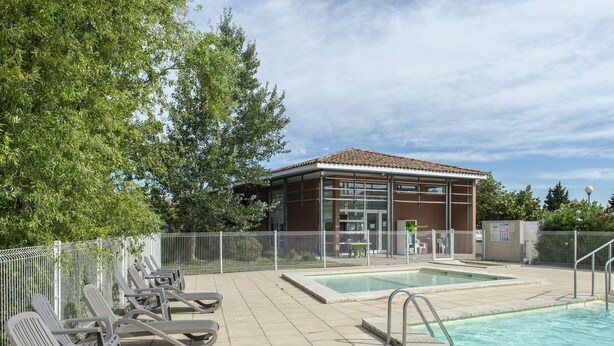 A swimming pool area with lounge chairs, a building with large windows, and a fenced garden. - Spacious Provence House for Eight (Saint-Saturnin-les-Avignon)