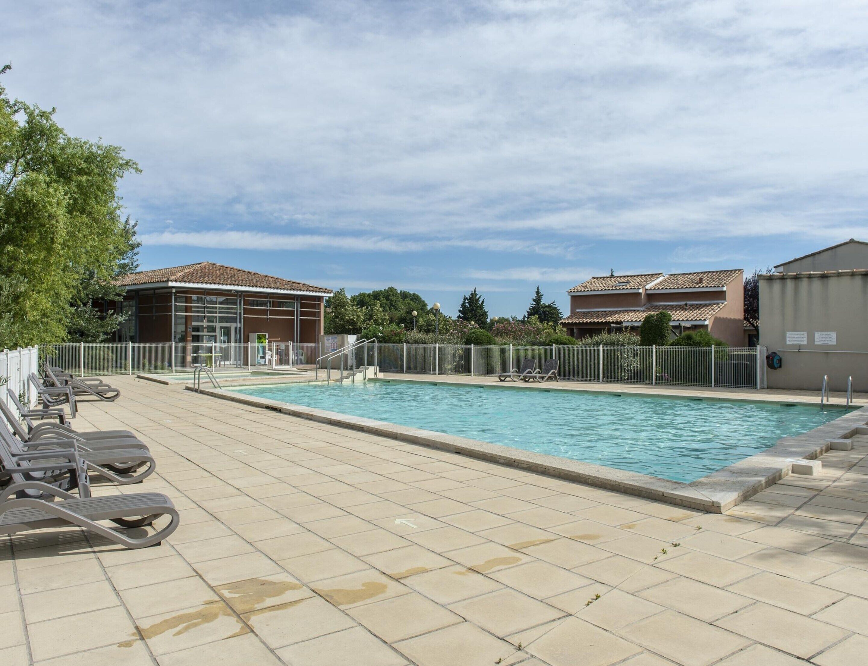 A swimming pool with sun loungers, a fenced area, and buildings with tiled roofs.