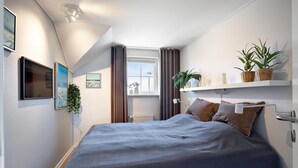 Une chambre à coucher avec un lit, une fenêtre, un radiateur, une étagère avec des plantes et un tableau au mur.