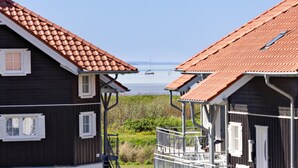 Deux maisons en bois aux toits recouverts de tuiles rouges, une vue dégagée sur la mer et un petit bateau aperçu au loin.