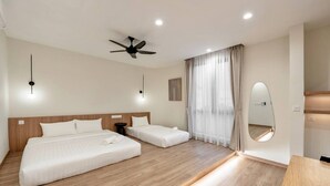 Habitación de hotel con dos camas, ventilador de techo, un espejo grande y suelo de madera.
