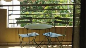 Un balcon avec une table et des chaises, une vue sur la verdure et un sol carrelé.