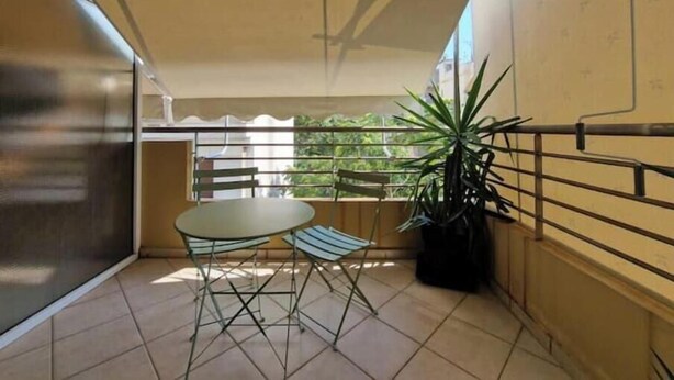 Un balcon avec une table et des chaises, un pot de fleurs et une vue sur la verdure.