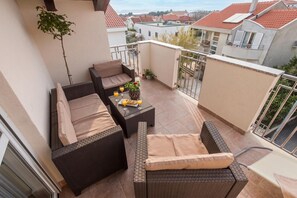 Un balcon agrémenté de meubles en osier, une petite table avec des boissons et une vue sur les immeubles voisins.