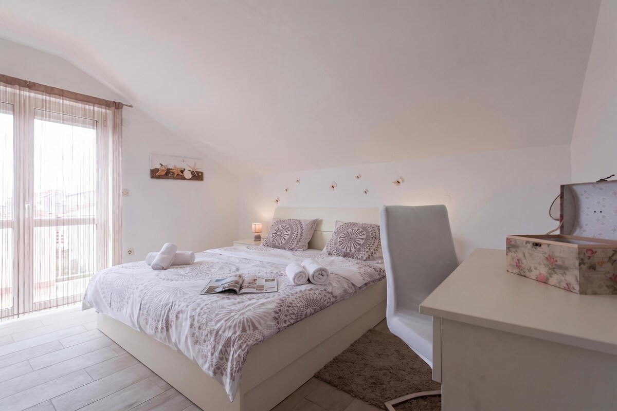 A bedroom with a bed, a desk, a chair, a window with curtains, and wall decorations.
