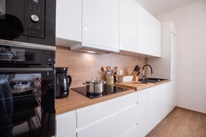 Une cuisine moderne avec des meubles blancs, un plan de travail en bois, un four encastré et une machine à café.