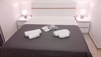 A neatly made bed with a dark bedspread, two white towels, and a magazine on the bed.