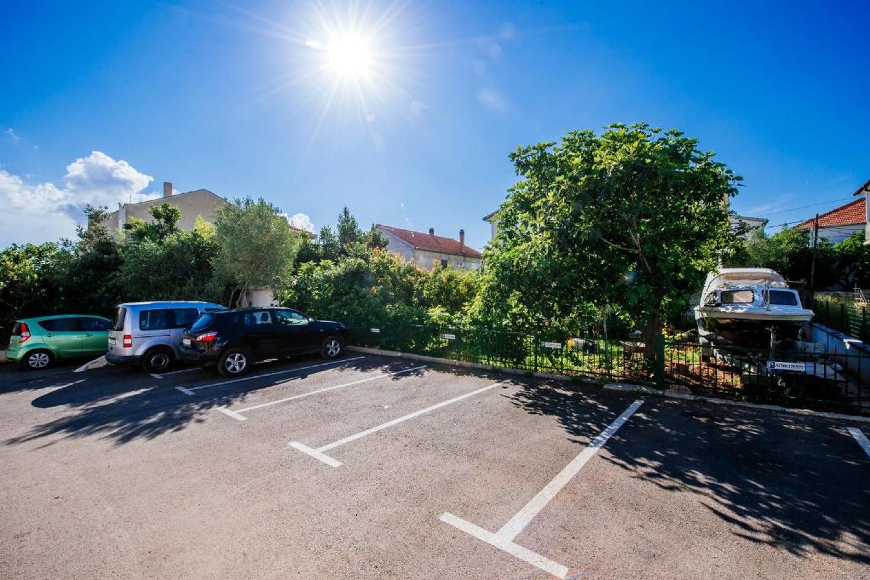 A parking lot with several cars, a boat, and a building in the background.