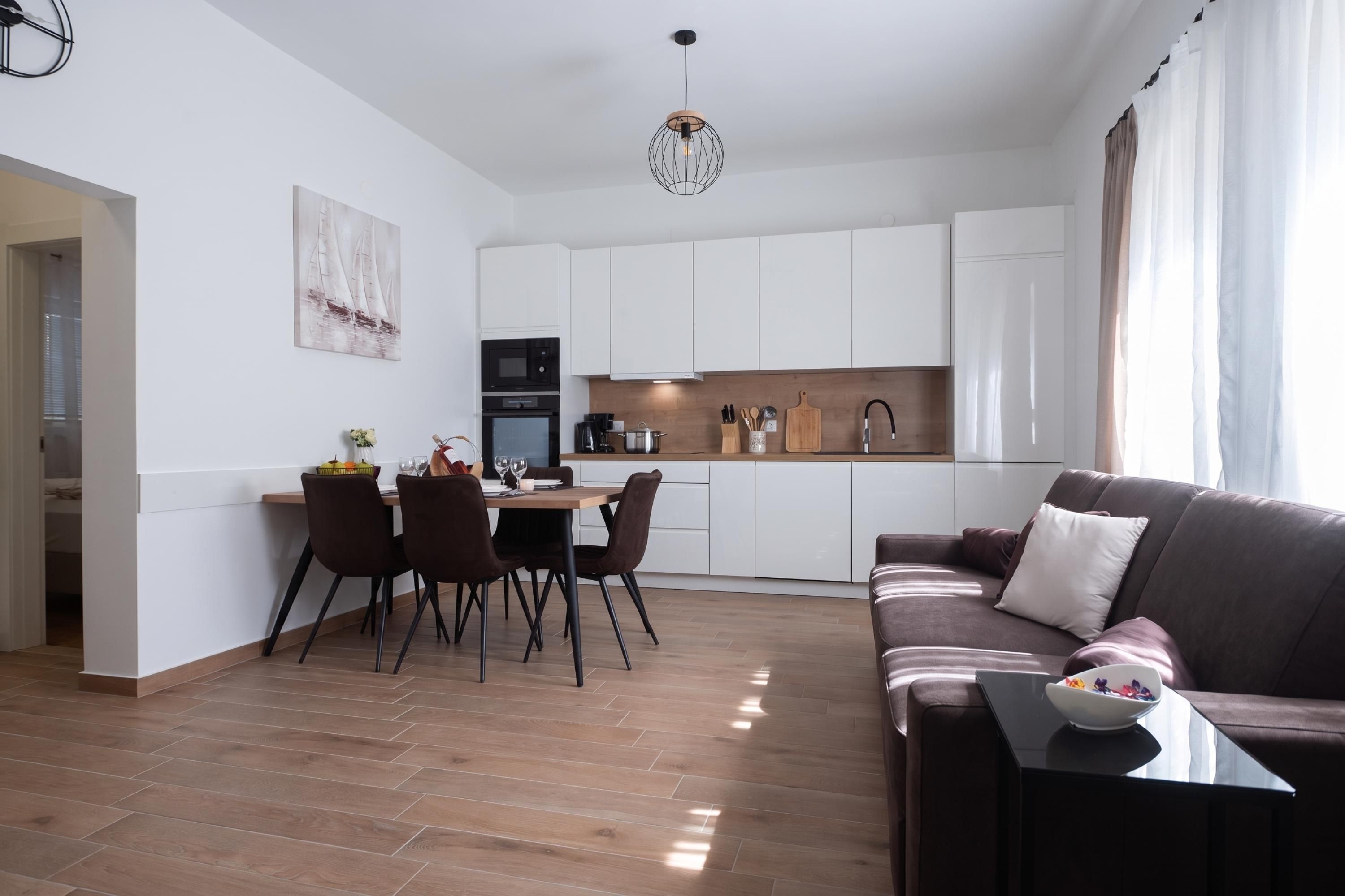 Une cuisine moderne avec des meubles blancs, un coin repas comprenant une table et des chaises, et un salon avec un canapé et une table basse.