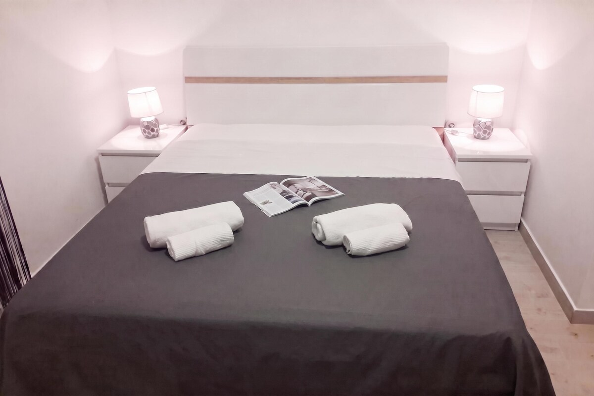A neatly made bed with a dark bedspread, two white towels, and a magazine on the bed.